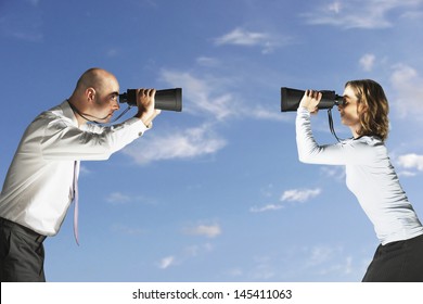 Side view of two business colleagues looking at each other through large binoculars against sky