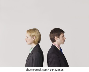 Side View Of Two Business People Standing Back To Back On Gray Background