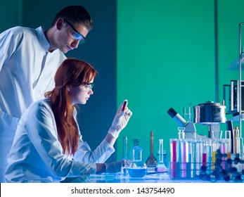 side view of two caucasian forensic scientists looking at a red cartridge with fingerprints on, in a laboratory