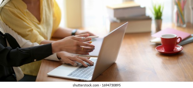 Side View Of Two College Girl Reading Together To Prepare Their Up Coming Exam With Laptop And Tablet In Comfortable Workspace