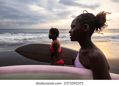 Side view of two confident and beautiful black girls walking on the beach with their surfboards in Sao Tome and Principe, Africa - Powered by Shutterstock