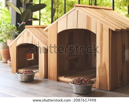 Side view of two empty wooden dog's houses with dog food bowls  in balcony decorated with houseplant in plant pot.
