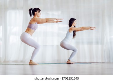 Side View Of Two Focused Girls In Shape In Awkward Yoga Pose. Yoga Studio Interior.