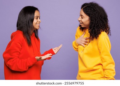 Side view two fun happy young little kid teen girls women they wear red yellow hoodie casual clothes talk to each other chit chat isolated on plain pastel light purple background. Lifestyle concept
