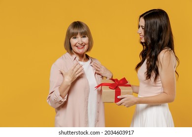 Side view two fun young surprised happy daughter mother together couple women in casual beige clothes gifting birthday present with red ribbon isolated on plain yellow color background studio portrait