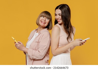 Side view two fun young daughter mother together couple women in casual clothes hold mobile cell phone stand back to back look to each other isolated on plain yellow background studio Family concept - Shutterstock ID 2142664673