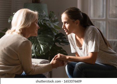 Side View Two Generations Mature 60 Years Old Mother And Millennial Grown Up Daughter Sitting Opposite Each Other, Holding Hands, Talking, Sharing Life Events, Discussing Relations Or Health Problems.