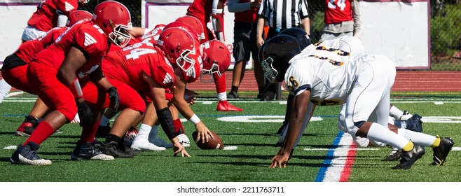 Side View Of Two High School Football Teams Lined Up For The Snap Of The Ball On A Green Turf Field.