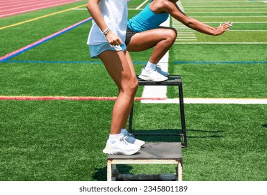 Side view of two high school girls jumping and landing on medal plyo boxes while training at practice on a turf field. - Powered by Shutterstock