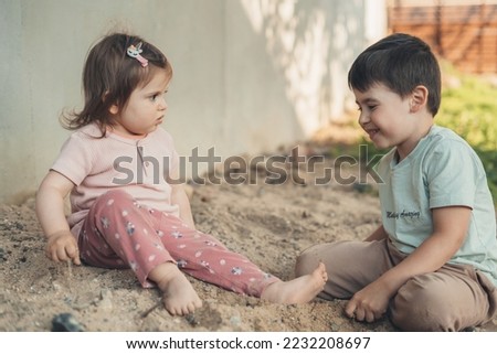 Side view of two kids sitdown on sandy ground and playing with sand in the home garden. People lifestyle. Happy family. Friends play.