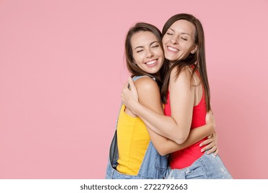 Side view of two pretty charming beautiful young women friends wear casual denim clothes posing standing hugging keeping eyes closed isolated on plain pastel pink colour background, studio portrait