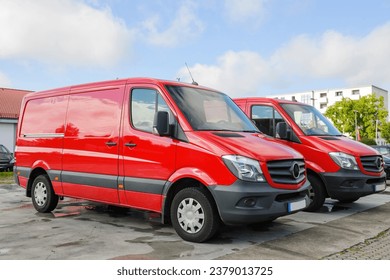 Side view of two red delivery vans parked in city center with blue sky with some scattered clouds above - logistic transportation delivery concept of goods and services