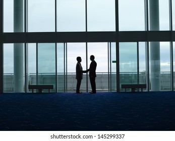 Side View Of Two Silhouette Businessmen Shaking Hands In The Airport Lobby