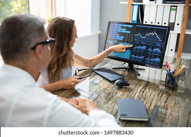 Side View Of Two Stock Market Brokers Discussing Graphs On Computer At Workplace - Powered by Shutterstock