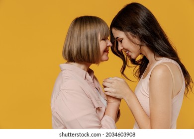 Side View Two Young Happy Lovely Smiling Daughter Mother Together Couple Women In Casual Clothes Hold Hands Touch Forehead Isolated On Plain Yellow Background Studio Portrait Family Lifestyle Concept.