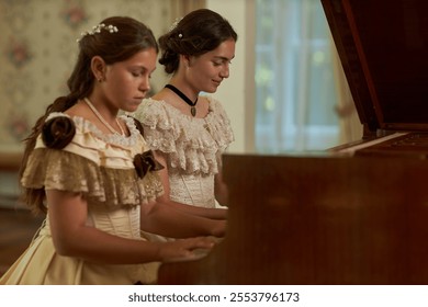 Side view of two young ladies playing piano duet wearing detailed lace dresses in warmly lit classic room, copy space - Powered by Shutterstock