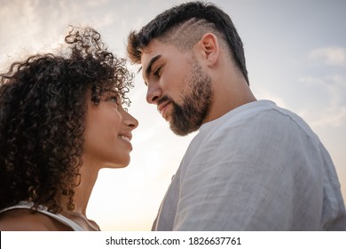Side view of two young multiethnic passionate lovers looking in the eyes each other - Macho bearded sexy man looks at his Latin woman with ardor in a romance sunset scene ideal for a book cover