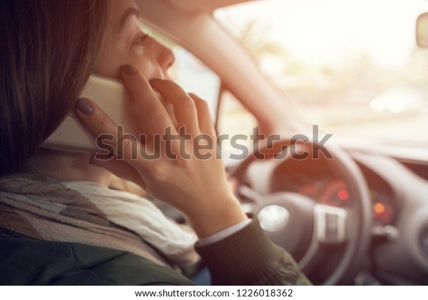 Side view unidentified\
female driver looking at road and talking on smartphone while\
driving in car