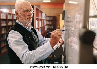 Side View Of A University Professor Writing Teaching In Class. Senior Lecturer Writing On Whiteboard In Classroom.