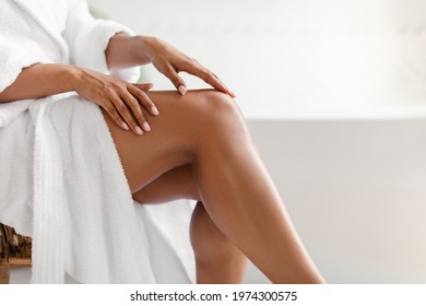Side View Of Unrecognizable Black Lady Touching Perfect Smooth Legs After Depilation Posing Sitting On Chair In Bathroom At Home. Cropped Shot Of Female Legs. Hair Removal And Body Care