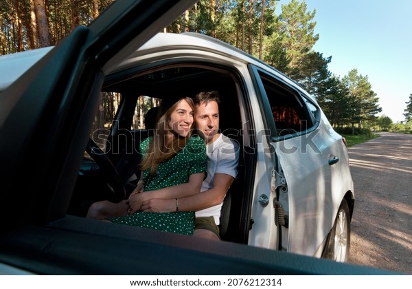 Side view of unrecognizable\
couple sightseeing in a car. Horizontal view of young couple\
traveling by car in forest landscape. Countryside travel and people\
concept