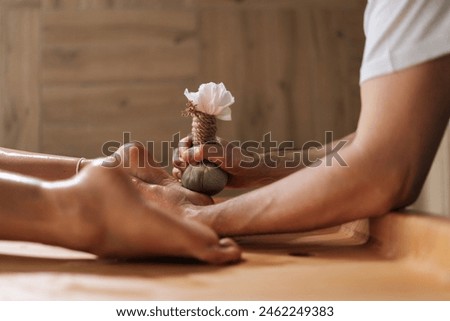 Side view of unrecognizable relaxed young woman getting Ayurvedic feet massage with Kizhi Herbal Bags by male masseur in luxury resort spa salon. Serenity of recreation at wellness center