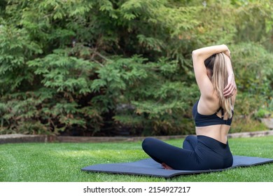 Side View Of Unrecognizable Young Woman Streching Her Arm In The Garden Wearing Back Top And Legging Sportwear