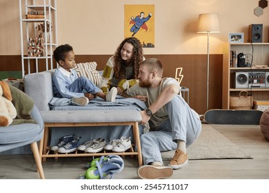 Side view of upset little Black boy sitting in bed while emotionally supportive parents talking to adopted kid in childs bedroom - Powered by Shutterstock