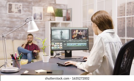 Side view of video editor working on a project from home. Boyfriend in the background is talking on the phone. - Shutterstock ID 1635272002