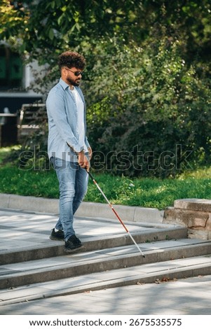 Side view, walking. Blind man with white cane and sunglasses is in the city.