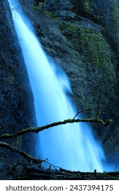 Side view of waterfall streaming between moss covered volcanic rock face.