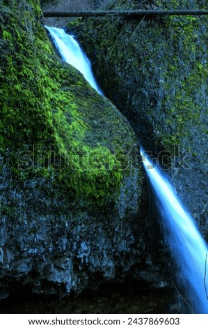 Side view of waterfall streaming between moss covered volcanic rock face. 
