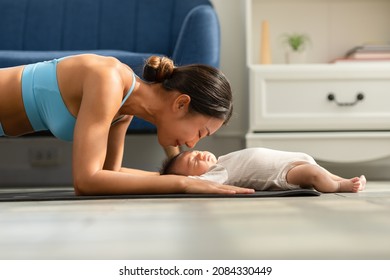 Side view of Wellness Asian woman mom doing plank exercise and kissing her baby at cozy home.Happy healthy mother yoga plank with newborn baby boy sleep and lying on yoga mat.Yoga Mom and Baby Concept
