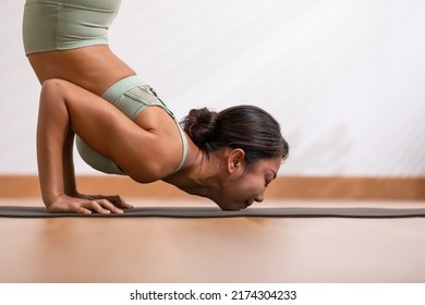 Side view of Wellness Asian woman wear green sportswear doing Yoga exercise,Yoga Chin stand pose Ganda Bherudasana.Calm of healthy activity young woman breathing and meditation with yoga at cozy home