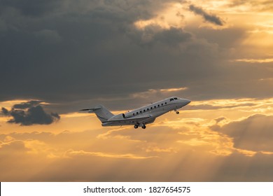 Side View Of White Business Jet With Turbofan Engines. Attractive Orange Cloudy Sunset Sky Over The Airport. Modern Technology In Fast Transportation, Business Travel And Tourism, Aviation.