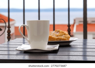 Side view of a white cup of tea and  plate with burek pastry on a balcony table with the view on  Adriatic sea in Makarska, Croatia on soft background.
