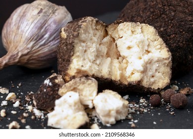 side view of a whole and broken ball of Belper Knoll cheese, black pepper and garlic lying on a black slate board. Hard Swiss cheese in the form of small balls in a sprinkle of black pepper. Close-up