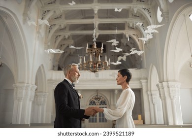 Side view wide angle portrait of senior couple as bride and groom holding hands in church interior, copy space - Powered by Shutterstock