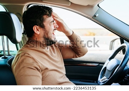 Side view wild cry and closed eyes, a hand on his forehead, a beard on his face, a headache. When the driver feels bad, it is better to stop moving and stop the car.