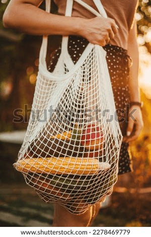 Side view of a woman arm walking and carrying white mesh string knitted shopping bag full of vegetables. Eco friendly, reusable shopping bag. Zero waste and