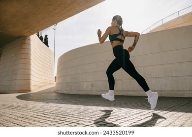 Side view of woman athlete is jogging on morning on modern building background. Healthy life concept - Powered by Shutterstock