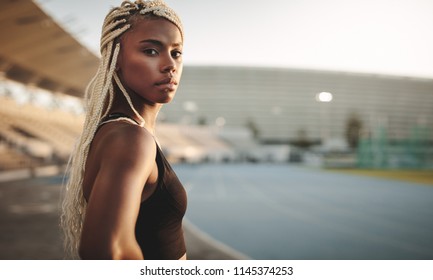 Side View Of A Woman Athlete Standing In A Track And Field Stadium Near The Running Track. Portrait Of A Female Athlete Standing In A Stadium.