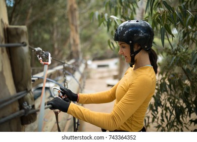 Side View Of Woman Attaching Carabiner To Rope Bridge