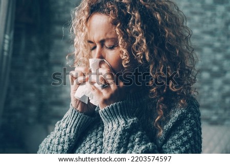 Side view of woman blowing nose for flu influenza symptoms in winter at home. Temperature reduction indoor to save energy gas costs. Female people with virus contagion using paper tissues. Disease