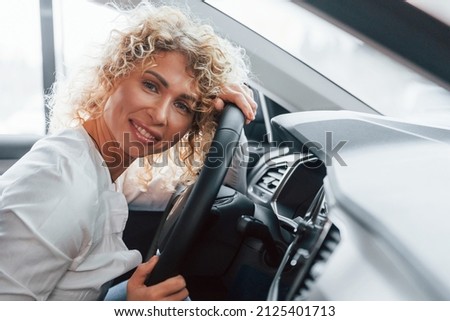 Side view. Woman with curly blonde hair is in autosalon.