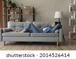 Side view woman enjoy day nap on comfy sofa. Young caucasian female put hands behind hear lying on cushion on cozy couch breath fresh conditioned air inside modern living room. Leisure, repose concept