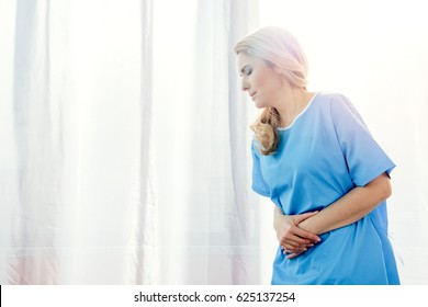 Side View Of Woman Feeling Stomach Pain In Hospital Chamber