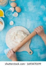 Side View Of Woman Hand Kneading Dough On Rolling Board With Rolling Pin And Water  Eggs On Blue Background With Copy Space