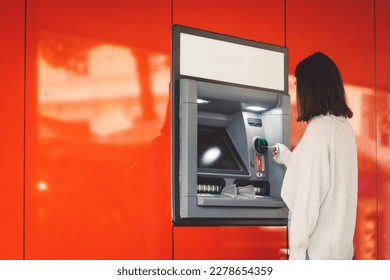 Side view of a woman inserting a card in the ATM on a red wall 