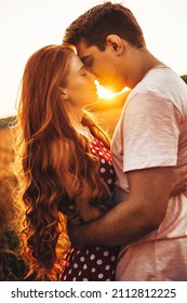 Side view of a woman with long red hair kissing her husband at an outdoor meeting. Posing against the bright background